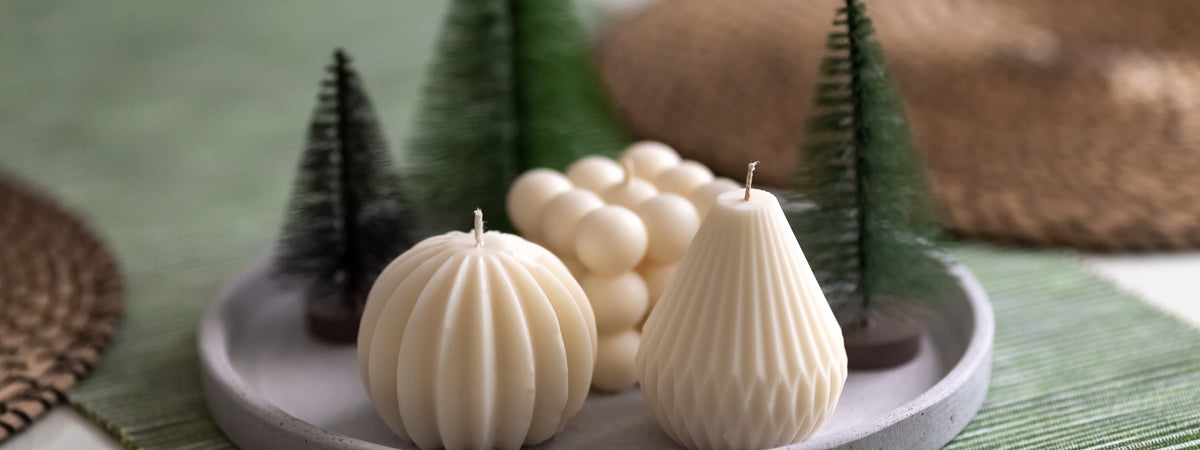 Cream sculptural candles arranged with miniature evergreen trees for elegant Christmas candle decor.