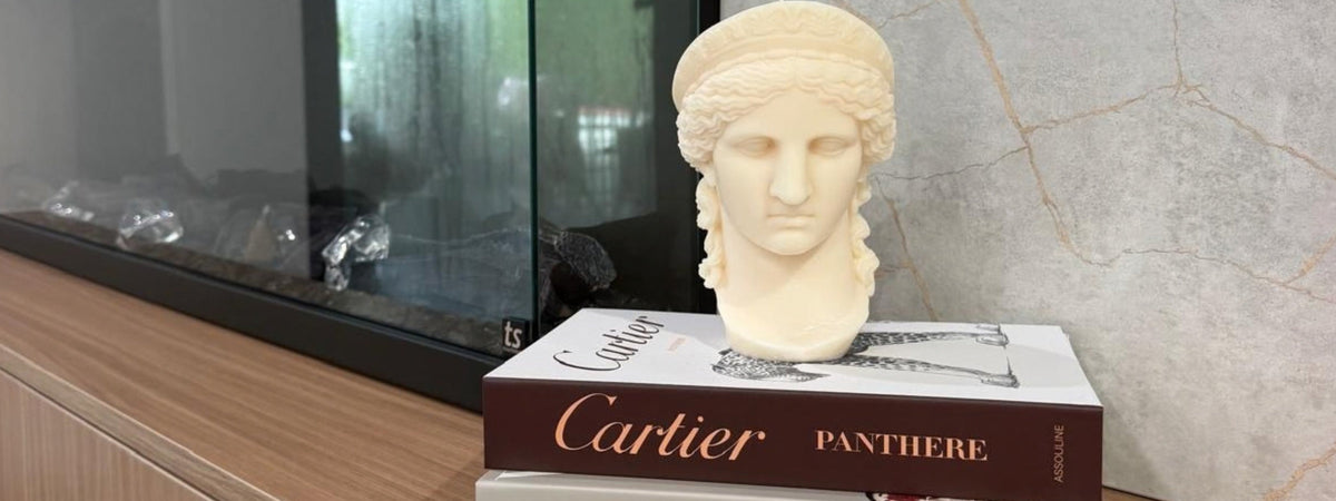 Ivory classical bust candle styled on stacked Cartier books beside a modern fireplace for a luxury candle gift guide.