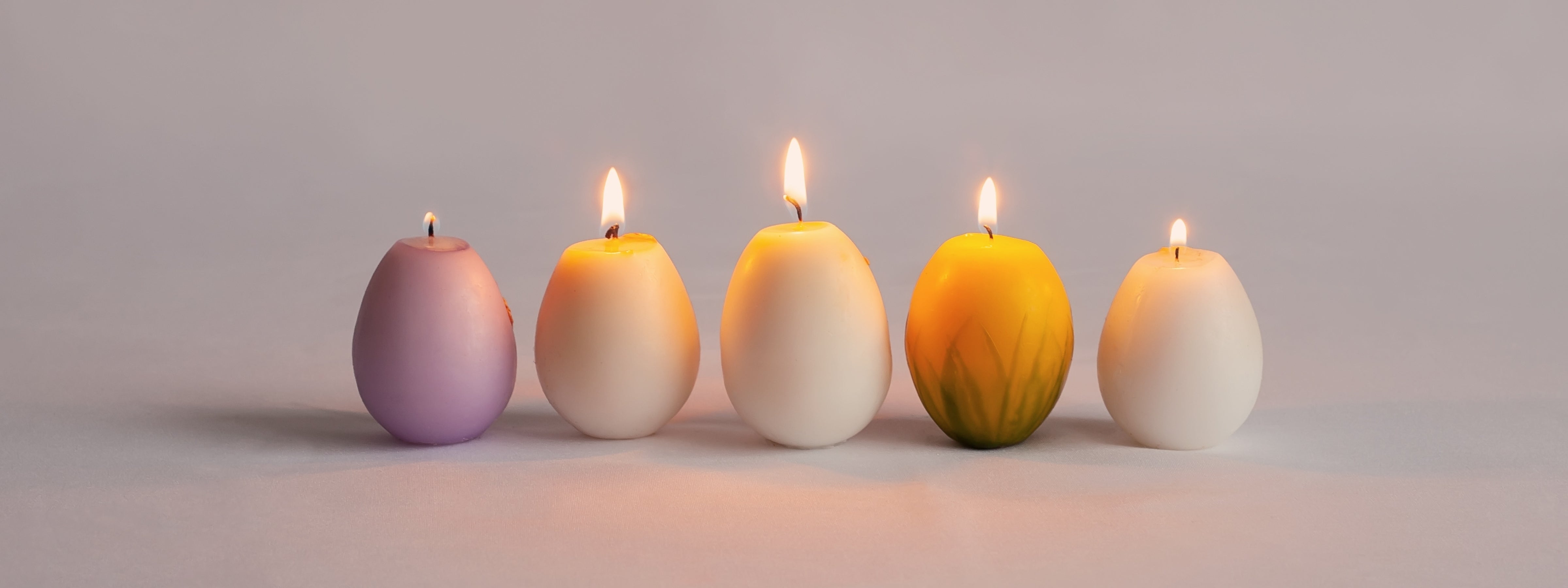 Five lit sculptural egg candles in soft spring tones arranged on a neutral background, creating a clean and elegant seasonal candle display.