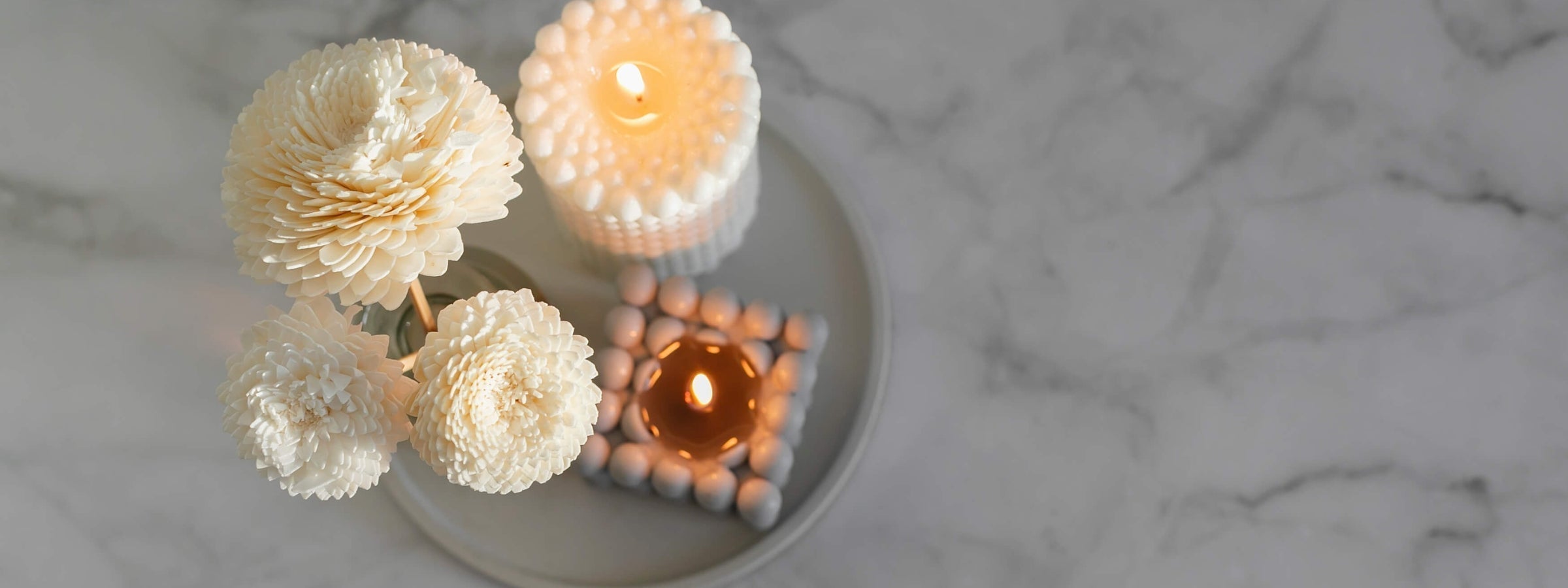 Minimalist candle arrangement with bubble candles and cream-colored flowers on a marble surface.