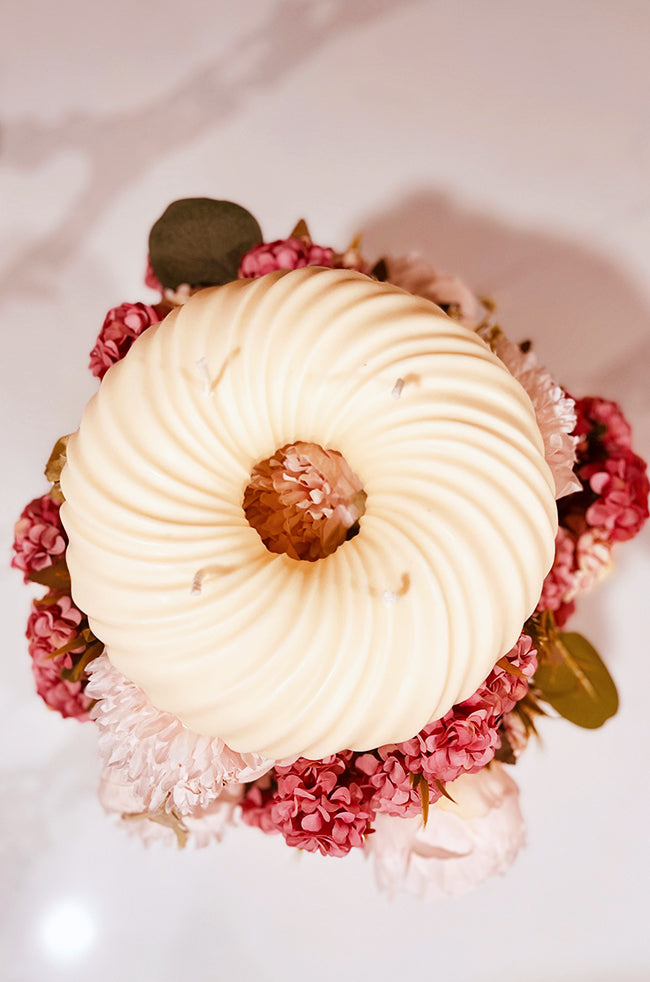 Groovy Donut Candle: Top view of an ivory grooved donut-shaped candle displayed on a bed of pink and red flowers.