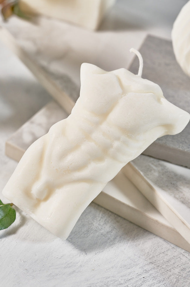 Adonis on Fire Candle: Sculpted candle in the shape of a male torso, featuring defined abs and a wick on top, placed on a neutral-toned surface.