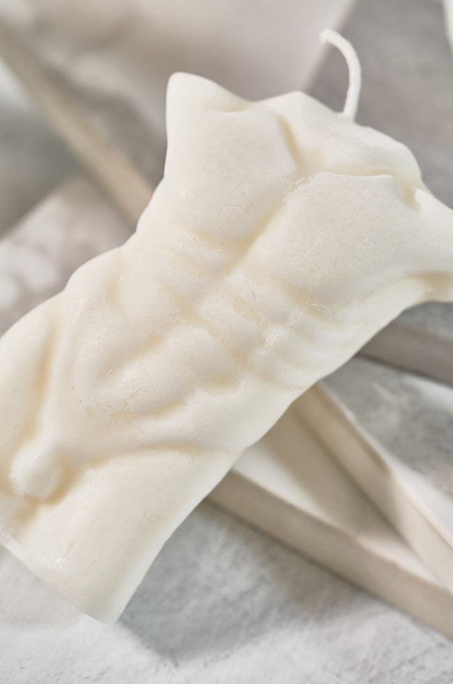 Adonis on Fire Candle: Sculpted candle in the shape of a male torso, featuring defined abs and a wick on top, placed on a neutral-toned surface.