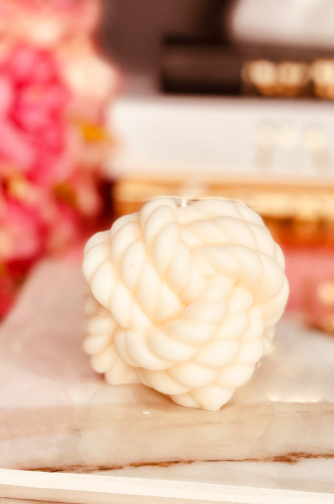 Alexanders Knot Candle: White sculpted candle in the shape of an intricate twisted knot, placed on a marble surface with a soft, elegant background.