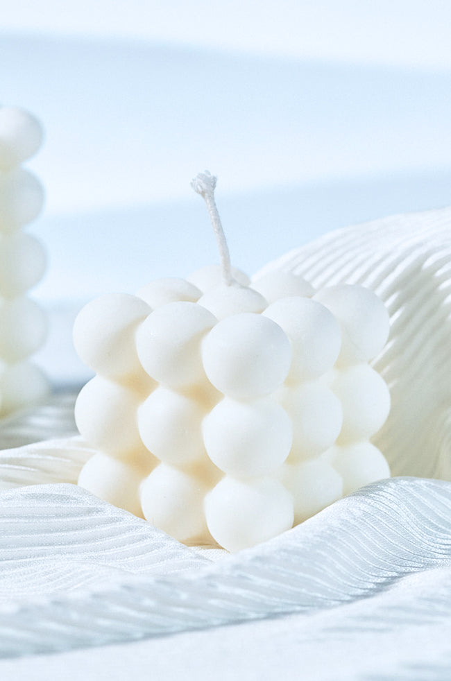 Bubble Candle Plain: A white bubble cube candle with a smooth, rounded surface pattern, placed on soft, white textured fabric under natural light.