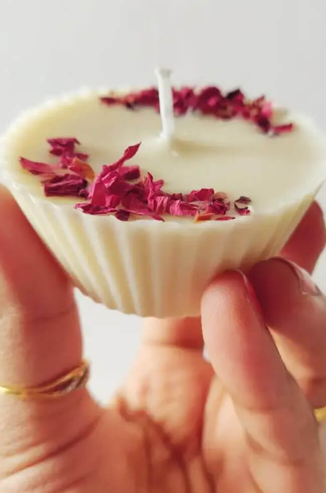 Cup Cake Candle: Hand holding a white cupcake-shaped candle topped with dried red flower petals, showcasing its detailed texture and elegant design.