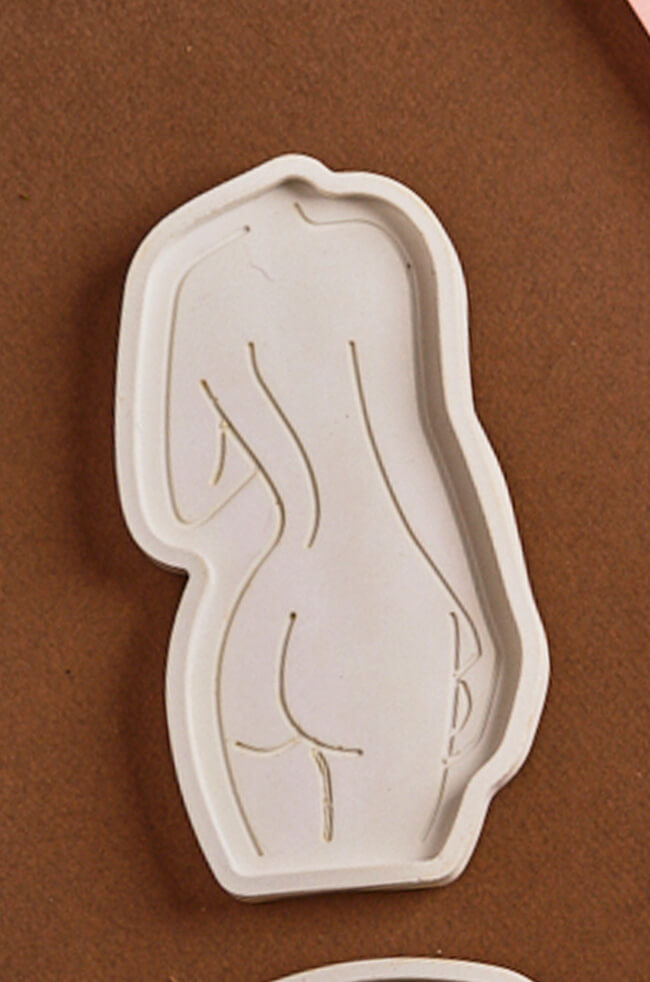 Daring Body Candle Tray: White sculpted candle tray in the shape of a female silhouette with minimalist line art detailing, placed on a brown surface.