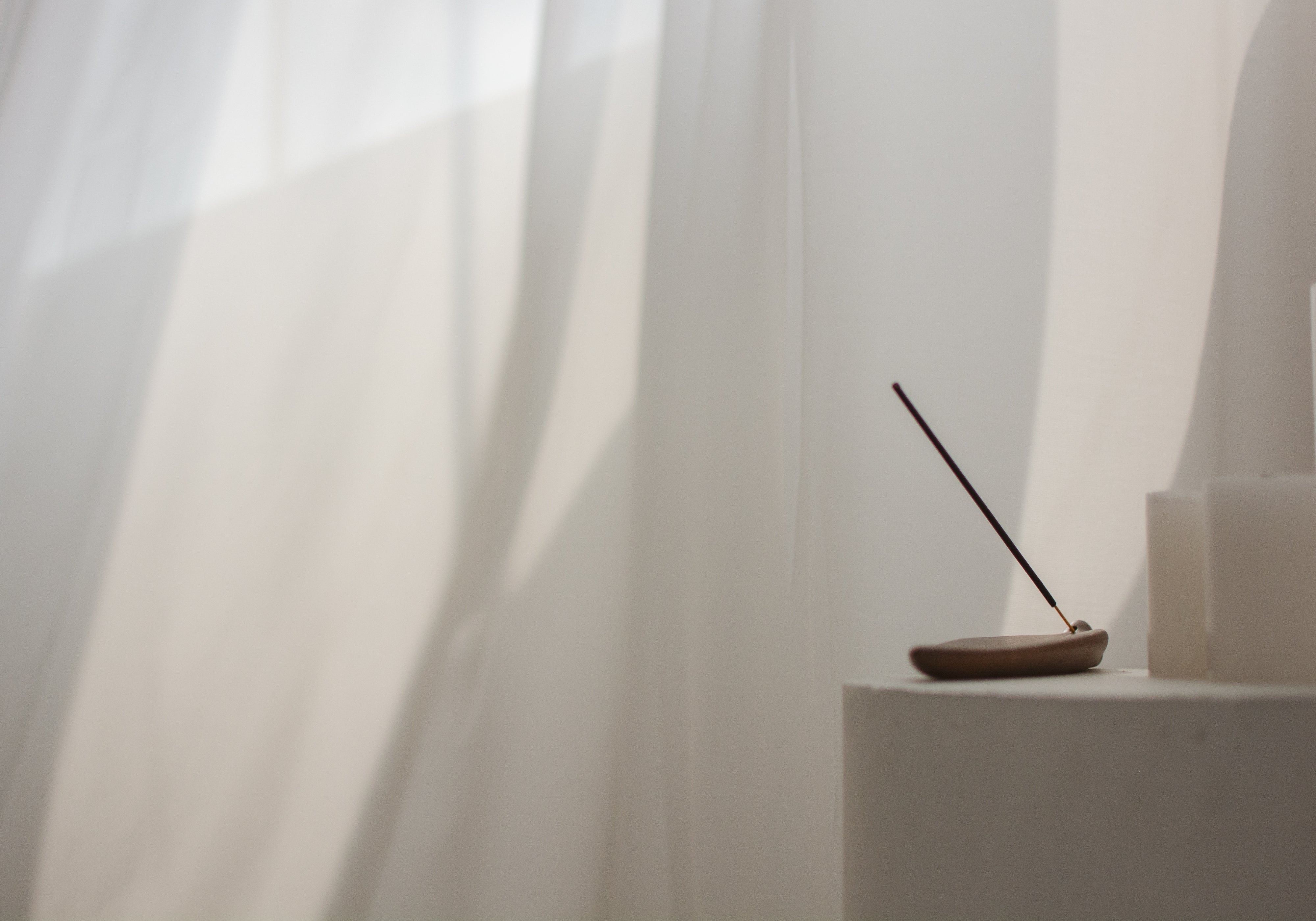 Minimalist incense stick burning on a neutral holder beside sculptural decor, creating a calm, earthy atmosphere.
