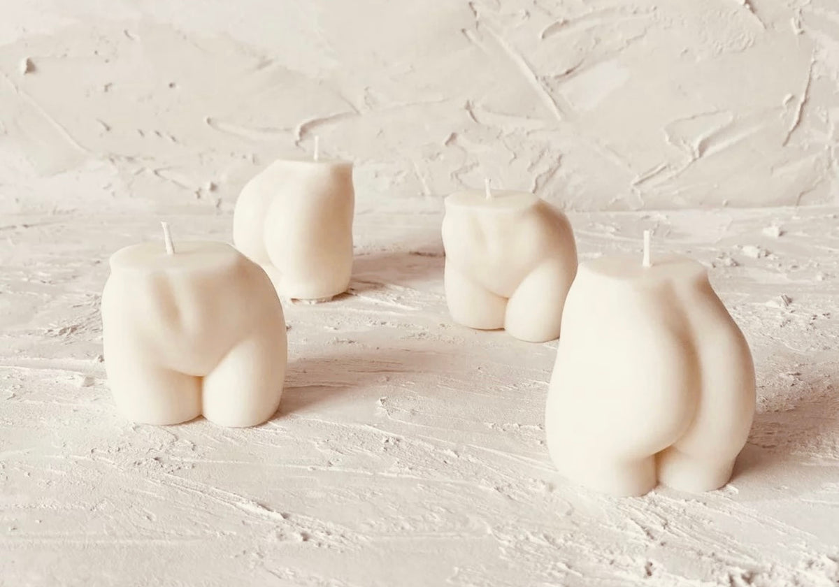 Four novelty body-shaped candles shaped like rear views, arranged on a textured off-white surface against a matching textured background.