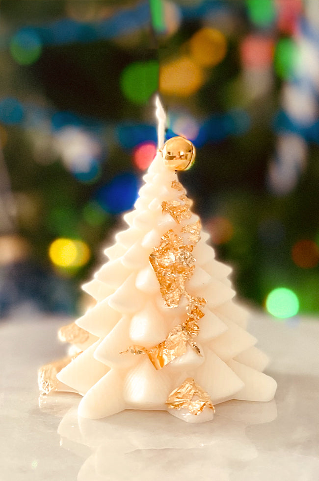 Fiery Tree Small Candle: White sculpted tree candle with delicate gold leaf accents wrapped around its layers, glowing softly against a warm holiday backdrop.