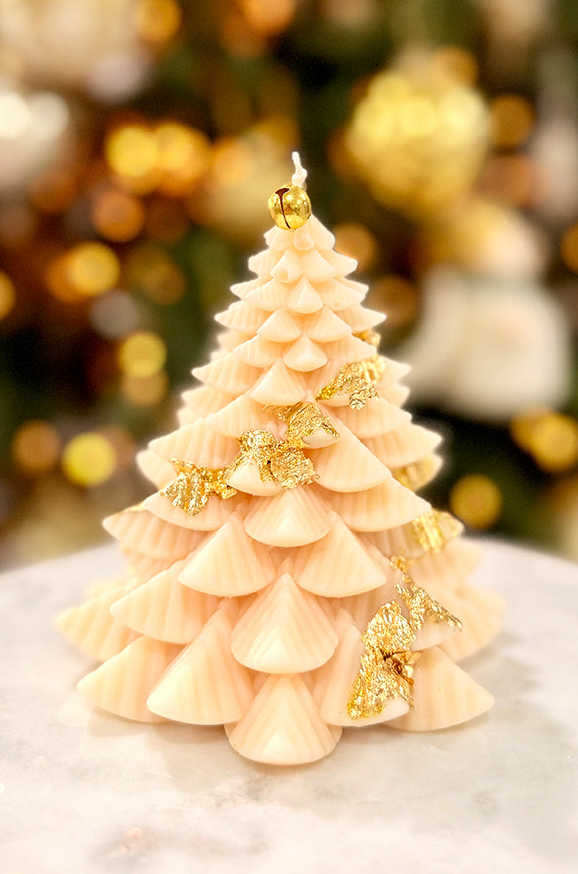 Fiery Tree Large Candle: Large ivory Christmas tree candle with layered sculpted branches, gold leaf accents, and a gold bell topper, displayed on a marble surface.