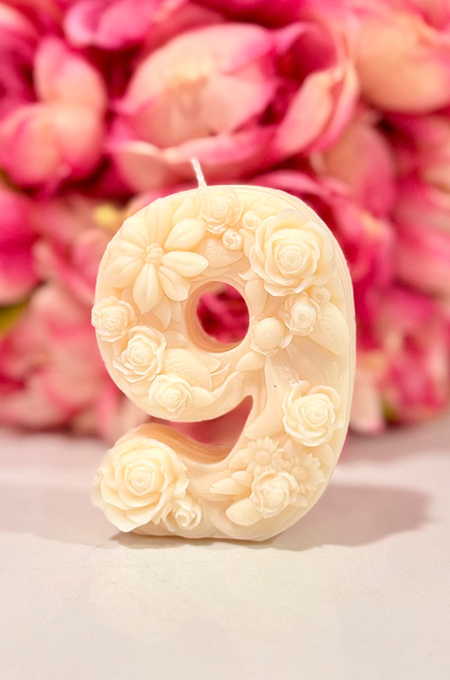 Floral Celebration Number Candle: Ivory floral number 9 celebration candle decorated with roses and delicate botanical details against a pink floral background.