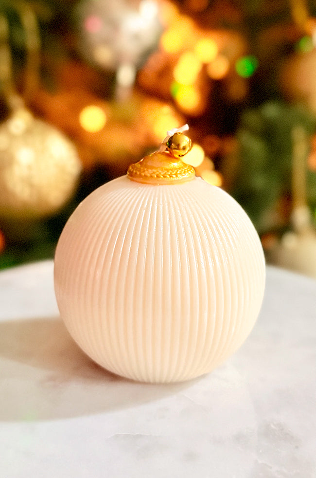 Golden Celestial Ornament Candle: A gold ornament candle with golden topper and ribbed design, illuminated by warm holiday lighting in the background.