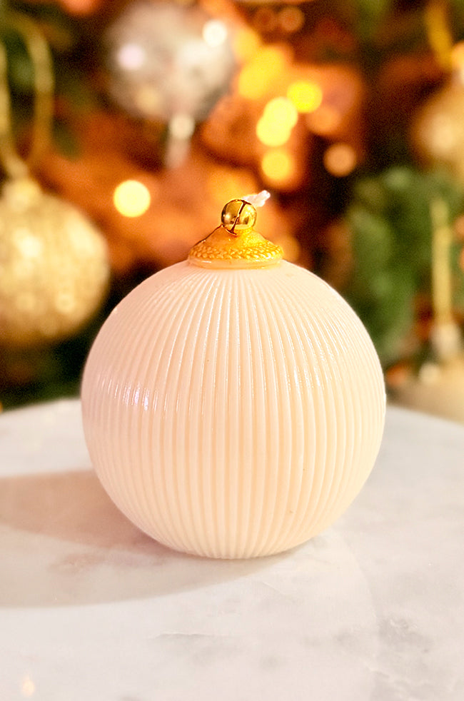 Golden Celestial Ornament Candle: Ribbed gold-white ornament candle featuring a gold bell at the wick, displayed with soft glowing Christmas tree lights.