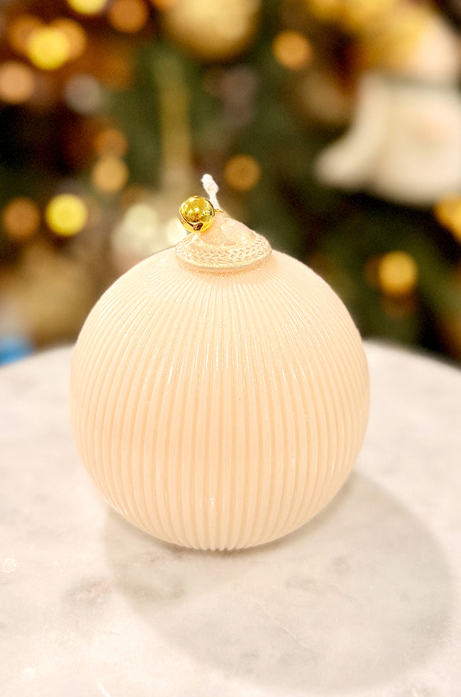 Golden Celestial Ornament Candle: Close view of a pearl ribbed ornament-style candle featuring a gold bell topper, set in front of glowing Christmas decor.