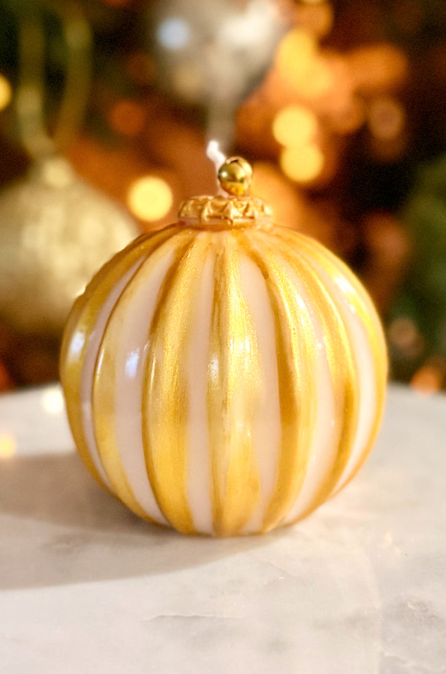 Golden Glow Ornament Candle: candle with ivory base, hand-painted gold vertical stripes, glossy finish, and gold bell topper on a marble surface.