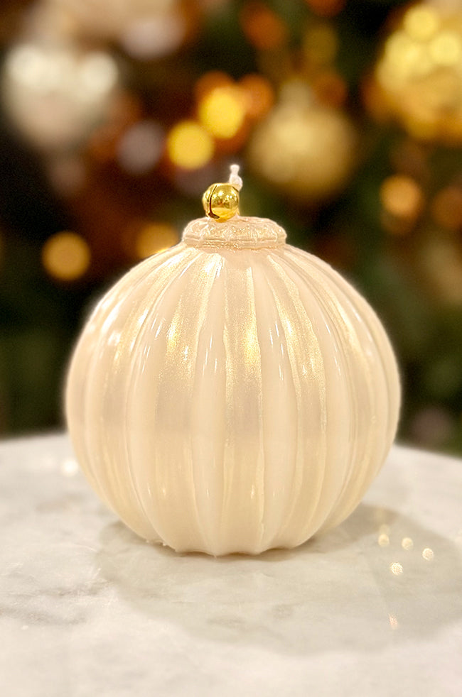 Golden Glow Ornament: candle with pearl ivory finish, ribbed texture, soft luminous sheen, and gold bell topper, displayed on a marble surface.