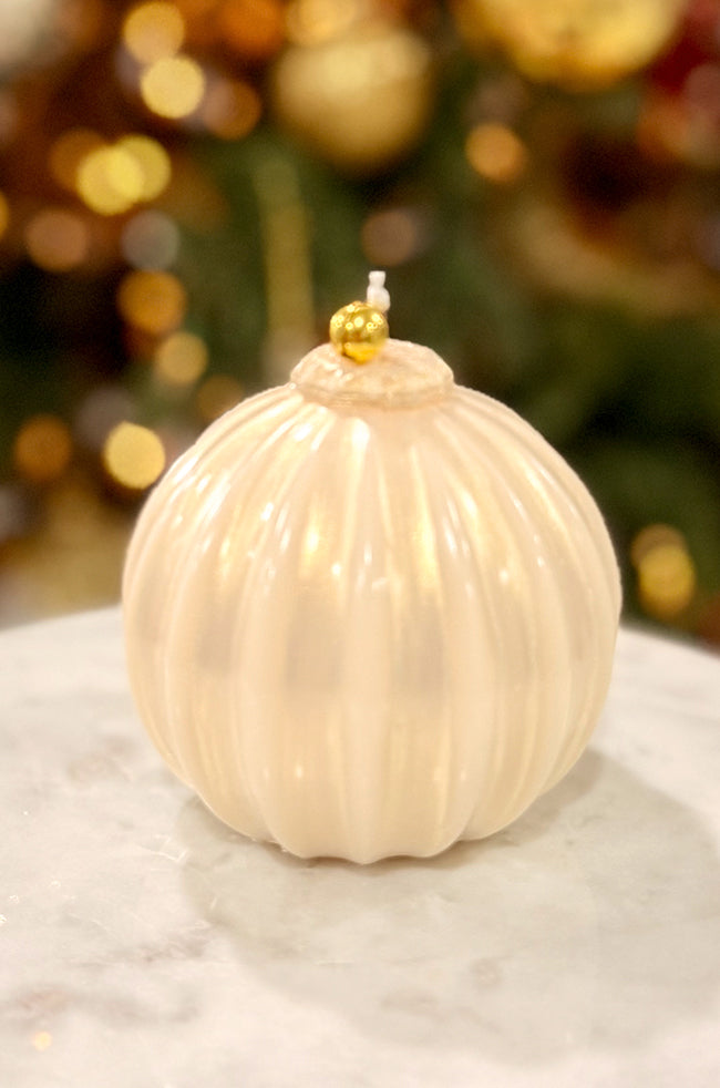 Golden Glow Ornament: Handmade pearl ivory ornament candle with subtle glow, vertical ribbed detailing, and gold bell topper, styled with warm holiday lighting.