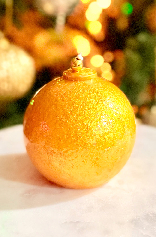 Golden Luxe Ornament Candle: Golden handcrafted ornament candle highlighted by warm Christmas tree lights, featuring a small bell at the top of the wick.