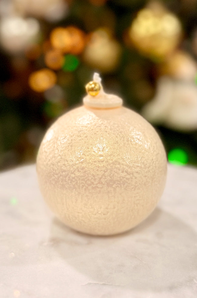 Golden Luxe Ornament: ornament candle with softly textured ivory finish, subtle shimmer, and gold bell topper, displayed on a marble surface.
