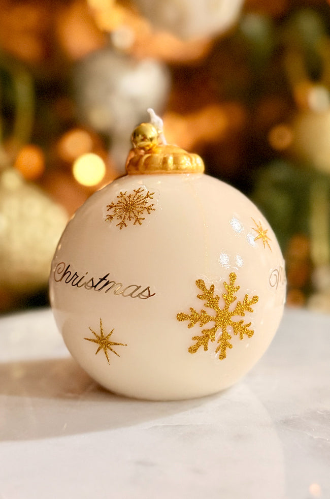 Golden Merry Ornament Candle: Handmade ivory Christmas ornament candle featuring gold snowflake details and a glossy varnished finish, topped with a golden bell, set against softly glowing festive décor.