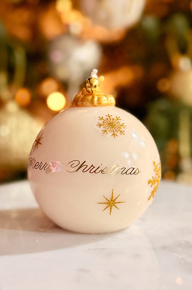 Golden Merry Ornament Candle: Luxury handmade Christmas ornament candle with gold snowflakes and “Merry Christmas” lettering, topped with a golden bell, photographed with warm festive lighting.