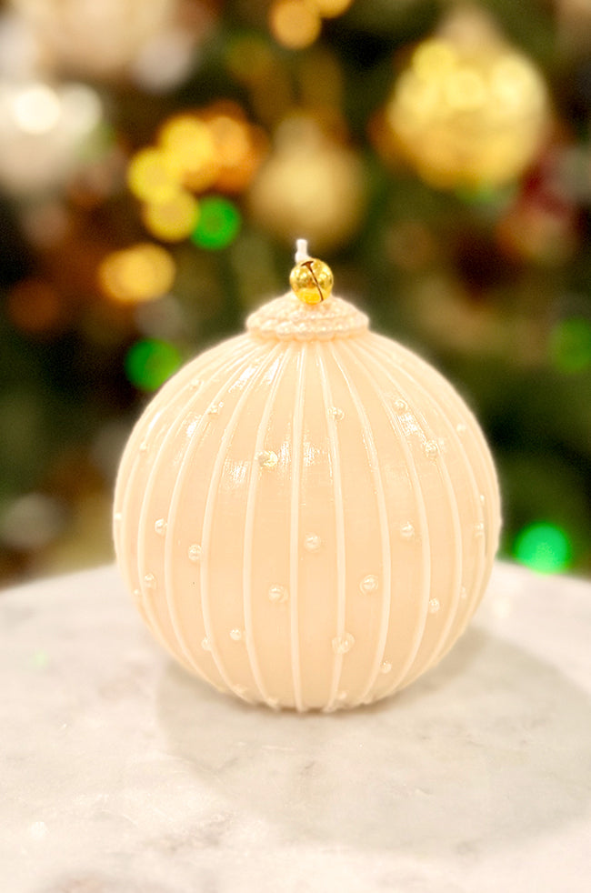 Golden Royale Ornament Candle: Handmade ivory ornament candle featuring pearl-style dotted details and a gold bell topper, styled in front of a softly blurred Christmas tree with glowing lights.