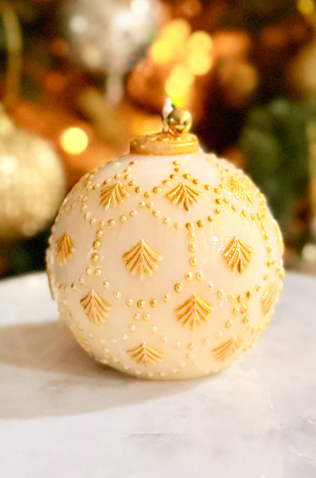 Golden Star Ornament Candle: Hand-poured ornament-shaped candle with hand-painted gold detailing and a glossy varnish finish, topped with a small golden bell, set against a festive blurred background.