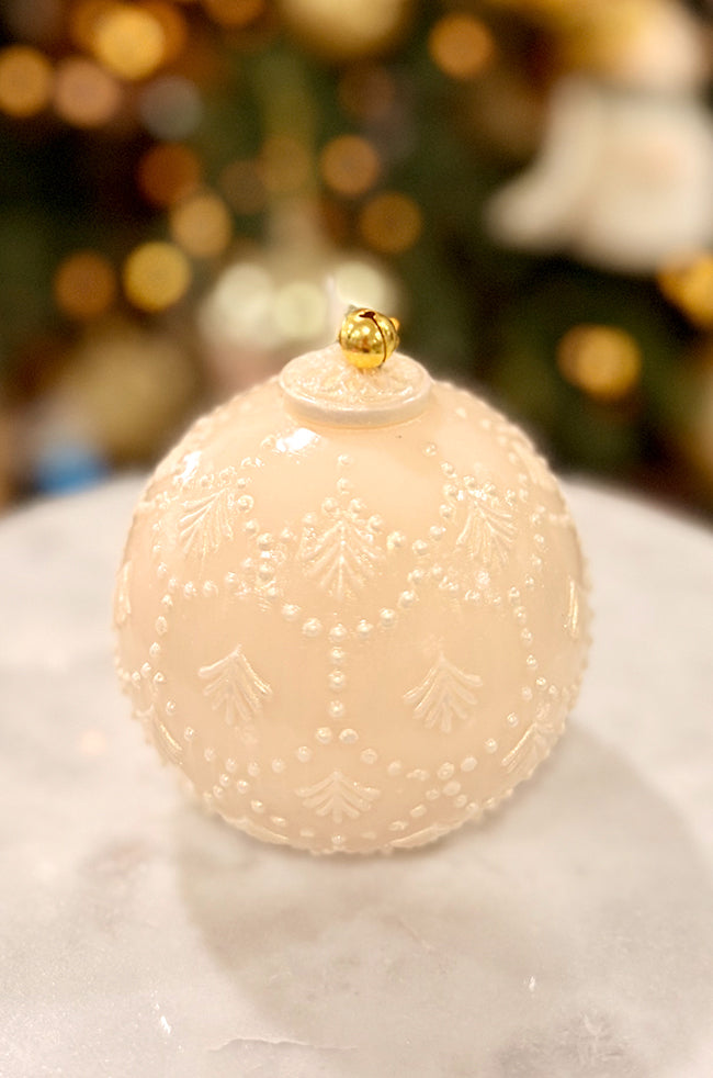 Golden Star Ornament Pear Candle: Pearl-colored spherical candle with intricate raised festive detailing and a gold bell topper, placed on a marble surface with glowing holiday lights in the background.