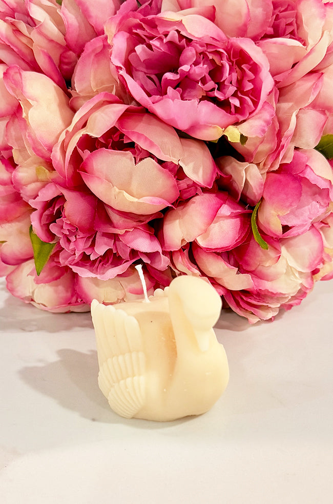 Grace Swan Candle: Front view of the handcrafted ivory Grace Swan candle with a bouquet of vibrant pink peonies in the background, emphasizing its graceful shape and luxury décor appeal.