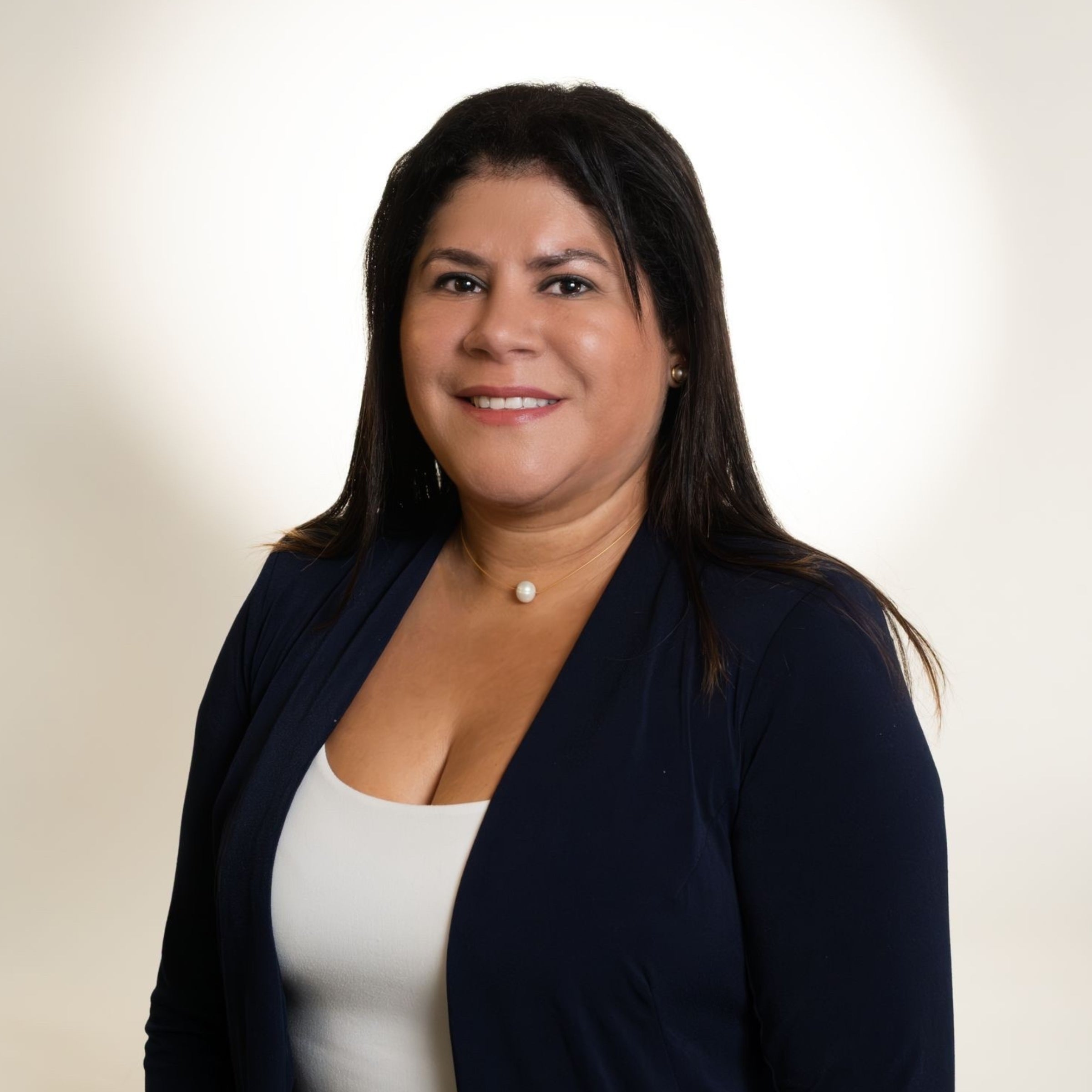 Portrait of Hilda Rodriguez, owner of Dahil Bar, smiling and wearing a navy blazer over a white top with a pearl necklace, set against a light background.