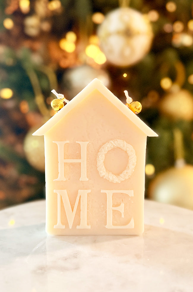 Home for Christmas Candle: Front view of the ivory Home for Christmas house-shaped sculptural candle with HOME lettering, wreath detail, and two golden bells on top.