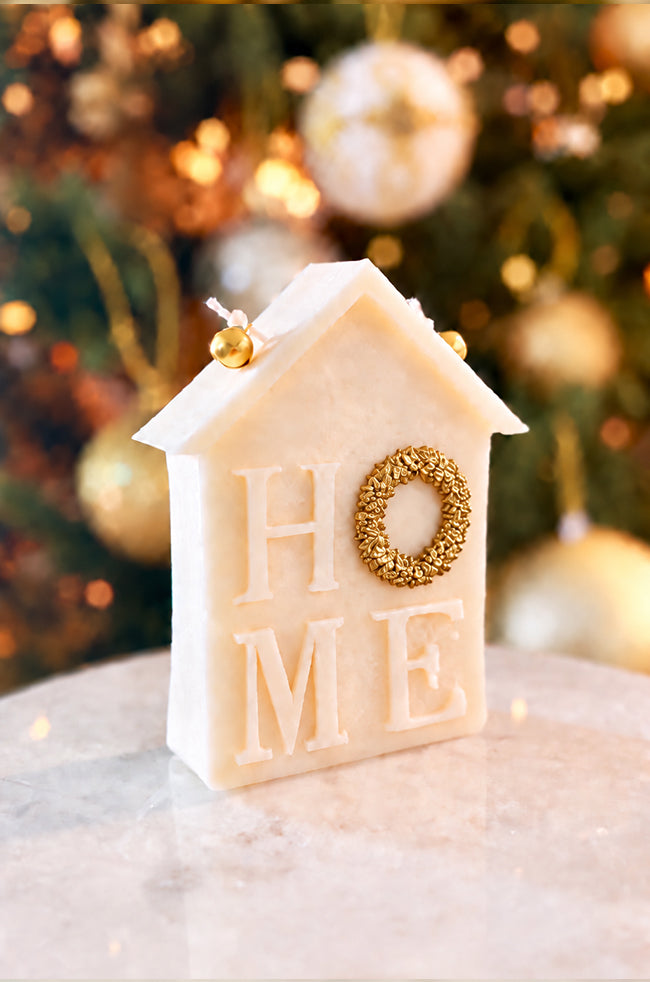 Home for Christmas Candle: Angled view of the Home for Christmas sculptural candle featuring HOME lettering, with a gold wreath detail and two golden bells against festive holiday décor.
