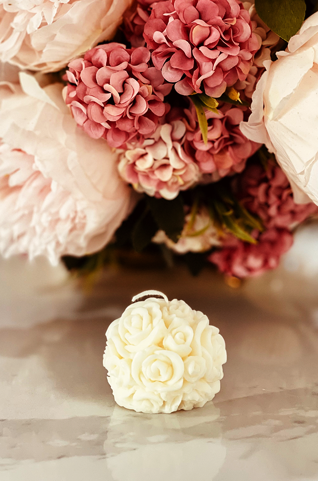 Mini Bloom Candle: White rose-shaped Mini Bloom candle surrounded by pink hydrangeas.