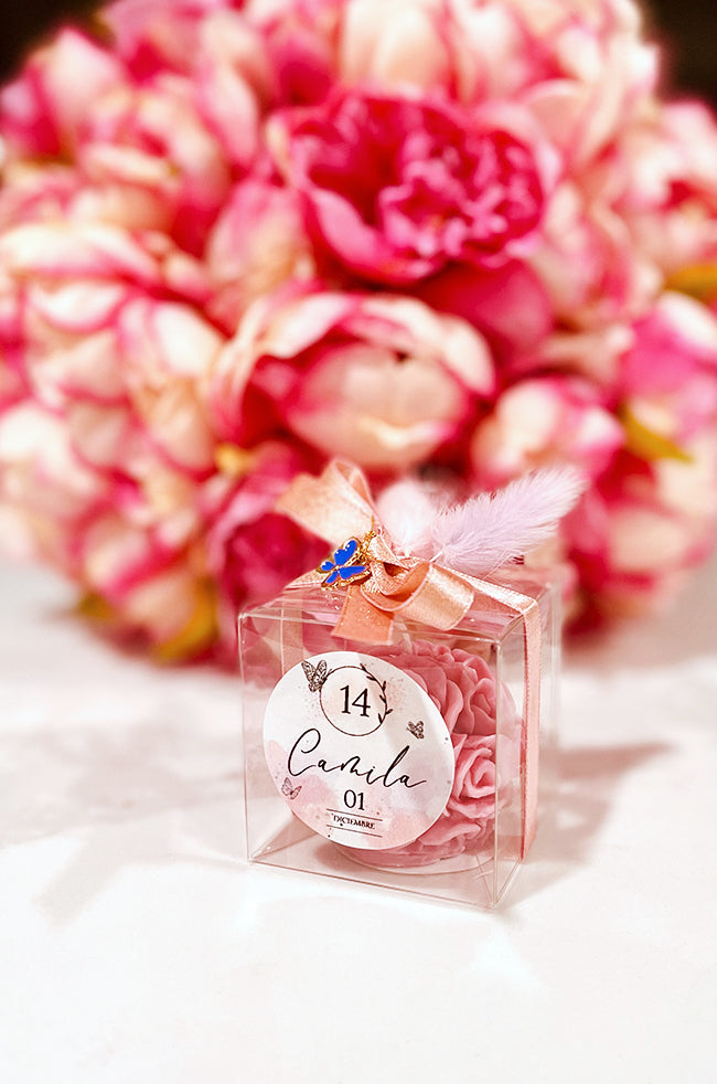 Mini Bloom Gifted: Pink Mini Bloom candle favor in clear box with rose-gold ribbon, butterfly charm, and custom label for Camila’s celebration.