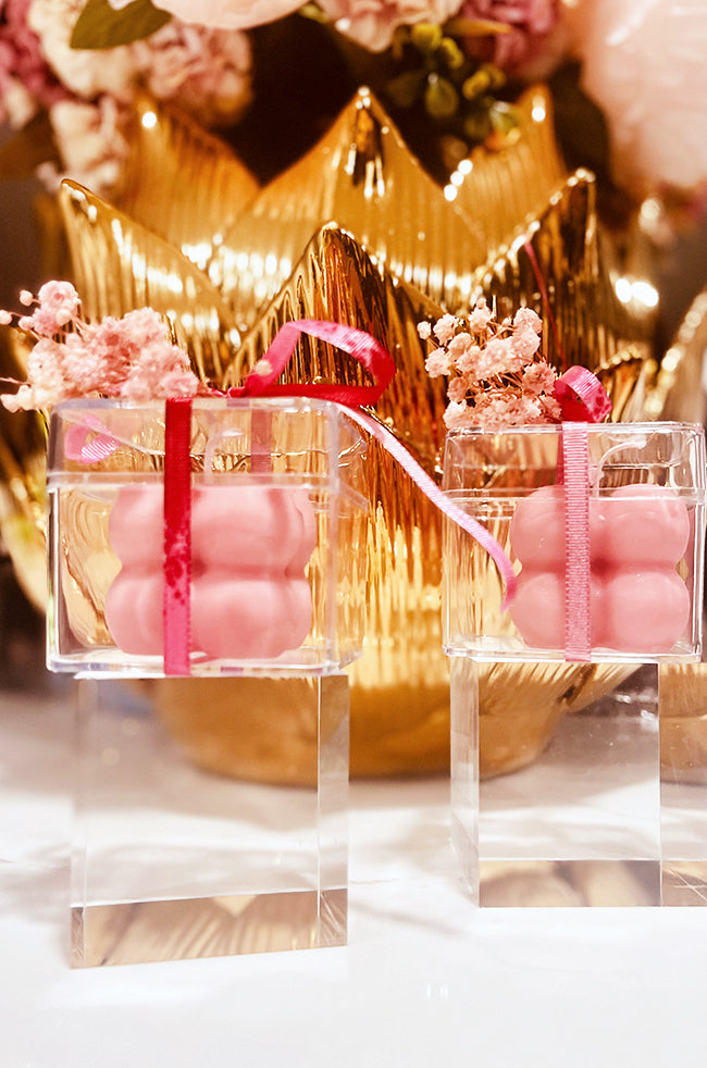 Mini Bubble Candle: Pink Mini Bubble candles in clear boxes with red ribbons and dried flowers, styled with golden decor.