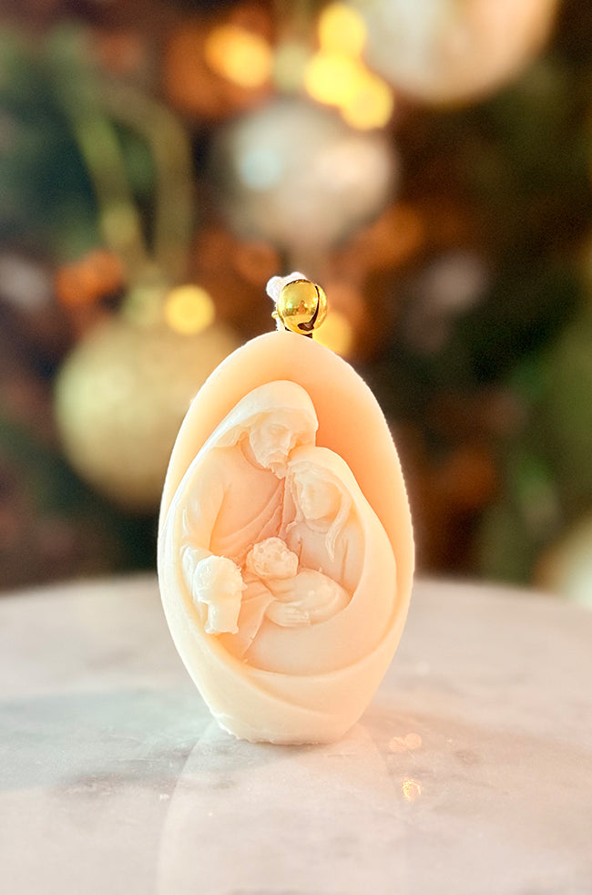 Nativity Glow Candle: Front angled view of the Nativity Glow sculptural candle with detailed Holy Family scene and gold bell against a festive holiday background.
