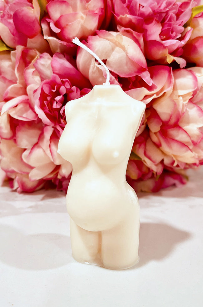 Pregnant Venus Candle: Ivory Pregnant Venus sculptural candle displayed in front of pink peony flowers.