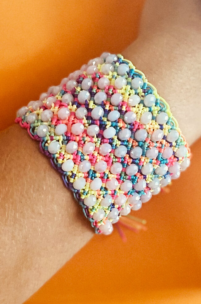 Pride: A vibrant handmade bracelet featuring pastel rainbow threads woven with glossy white beads, creating a colorful, textured pattern with a playful and cheerful look.
