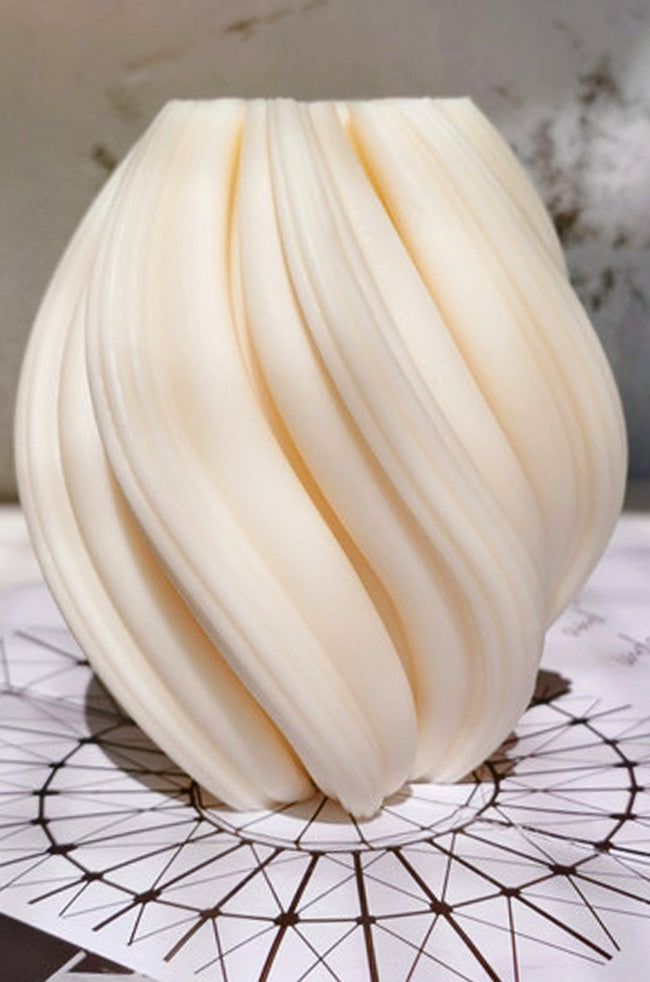 Rising Column Medium Candle: ivory sculptural candle with modern twisted curves displayed on a marble surface with pink floral décor.