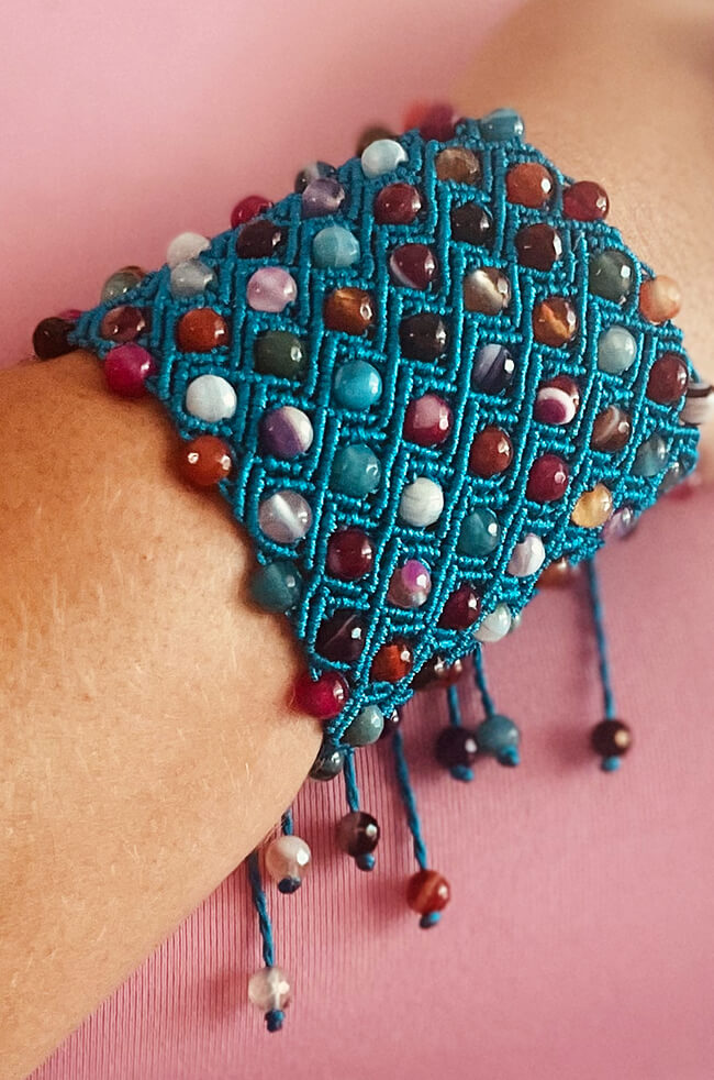 Sapphire: A handmade bracelet featuring a grid of multicolored round beads intricately woven into a vibrant turquoise thread, with dangling bead-tipped tassels adding a playful finish.