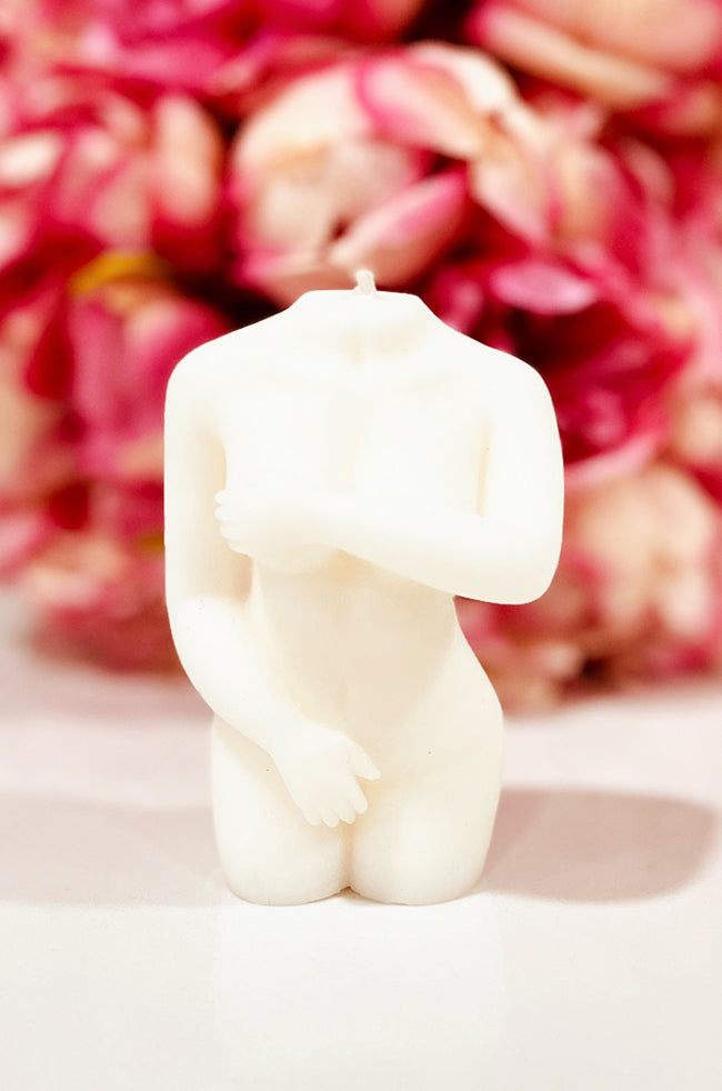 Shy Lady Candle: Ivory Shy Lady candle with a graceful crossed-arm pose, styled in front of vibrant pink flowers.