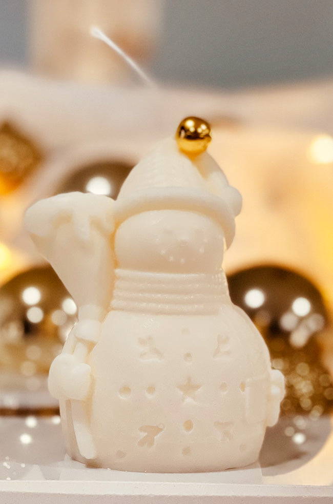 Snowman Candle: Ivory Snowman sculptural Christmas candle with festive cutout details and a gold bell on top, styled with warm gold holiday ornaments.