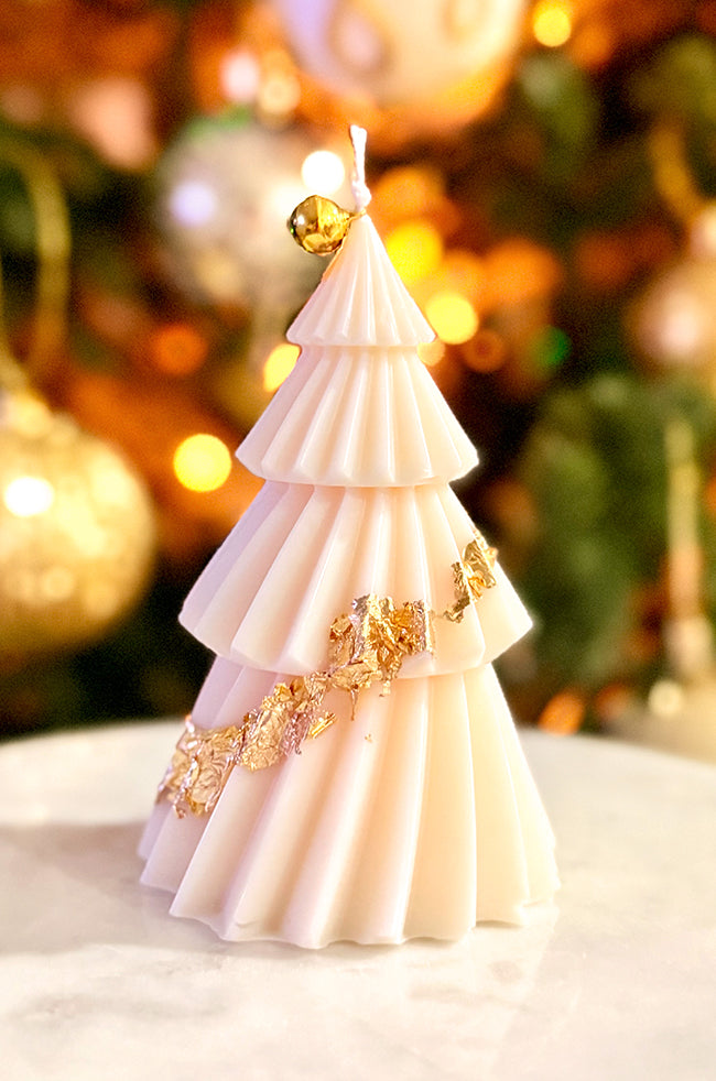 Solstice Tree Large Candle: Luxurious handmade Solstice Tree candle with a minimalist folded design and gold bell accent, surrounded by glowing holiday lights.