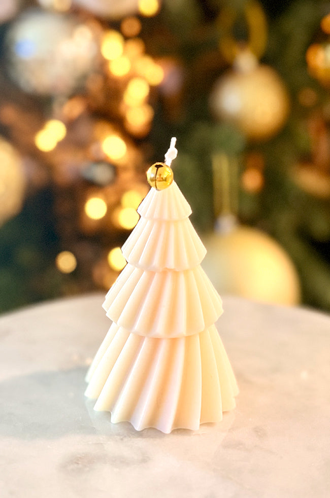 Solstice Tree Small: A sculpted cream-colored candle shaped like a tiered Christmas tree, topped with a gold jingle bell, set against a softly glowing holiday background.
