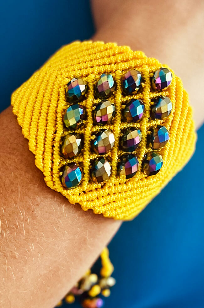 Sunshine: A vibrant yellow handmade bracelet featuring a grid of iridescent faceted beads and detailed macramé-style stitching, worn on the wrist against a blue background.