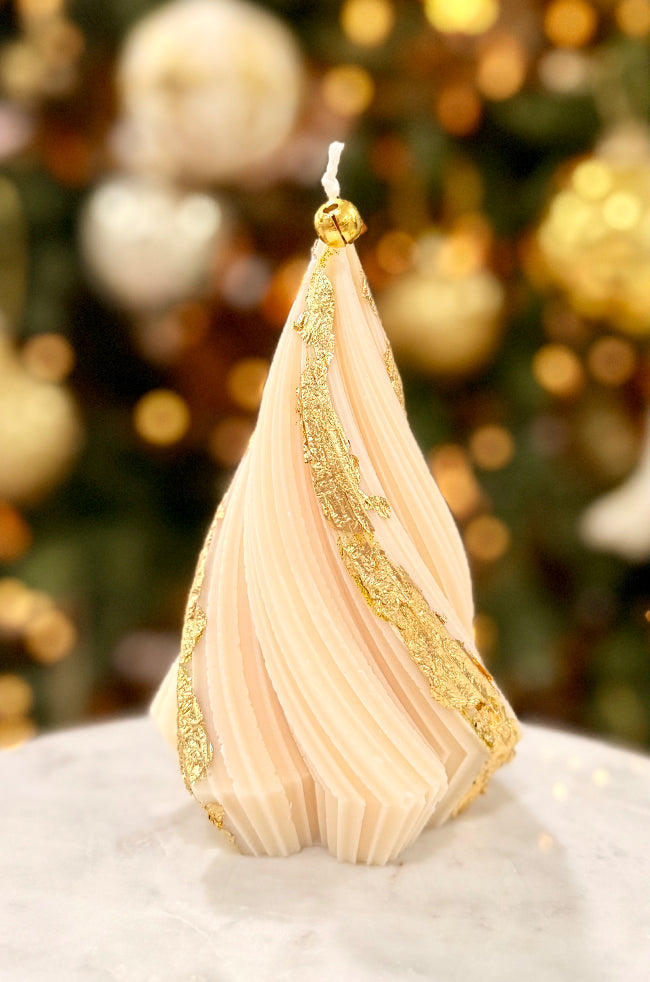Swirling Fir Tree Large Candle: Hand-poured white sculptural candle with gold flake accents resembling a spiraled fir tree, featuring a golden bell on the wick, staged with reflective gold ornaments and a cozy holiday ambiance.