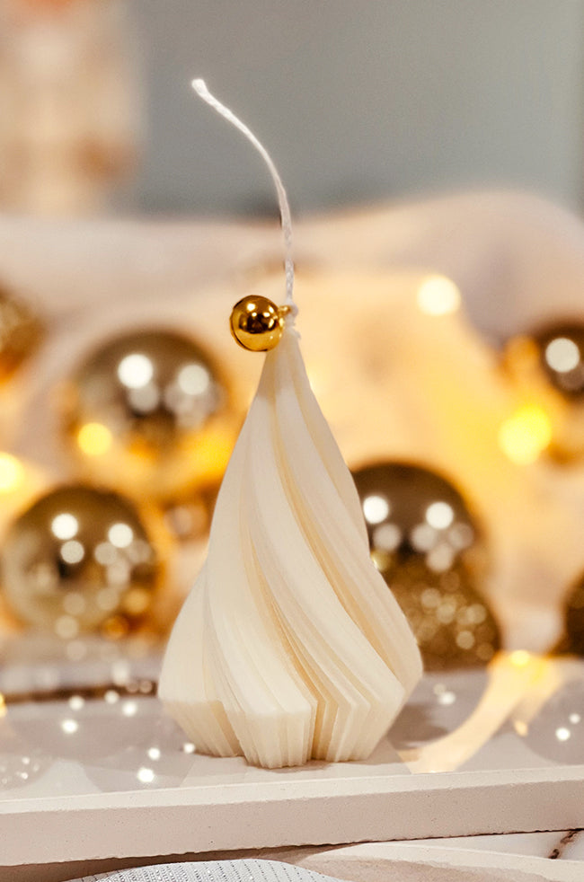 Swirling Fire Tree Small Candle: Hand-poured sculptural candle shaped like a swirling fir tree with a gold bell on top, styled among gold ornaments for the holidays.