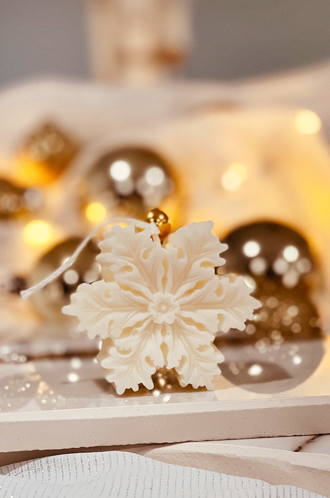 The Christmas Snowflake Candle: Ivory Christmas Snowflake sculptural candle with intricate floral details and gold bell, styled with warm holiday décor.