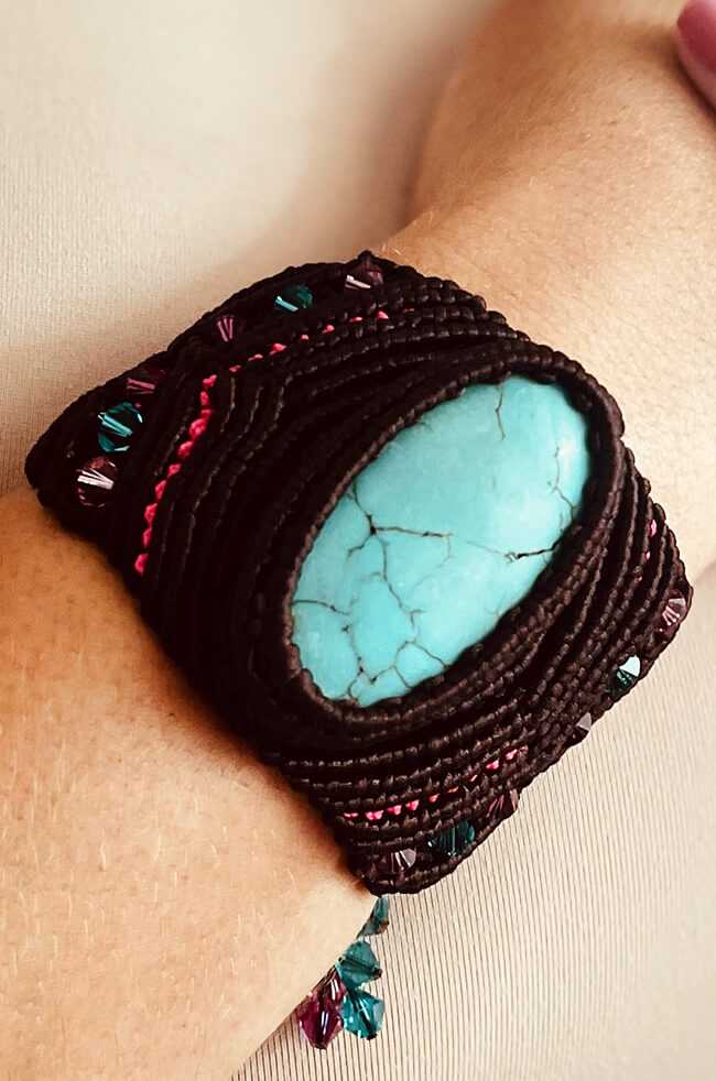 Turquoise: A handcrafted bracelet featuring a large turquoise stone centerpiece set in dark brown macramé with accents of pink, teal, and purple beads, worn on the wrist.